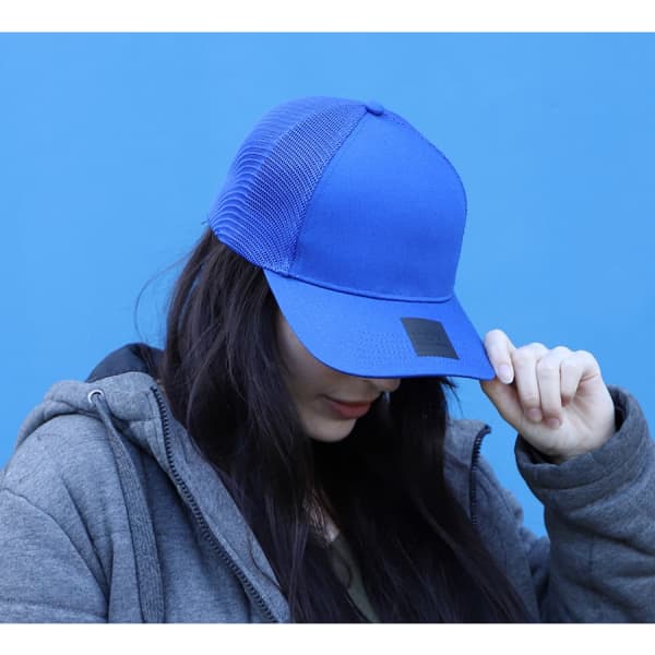 A blue cap with a mesh back and a logo, worn by a person with long dark hair, set against a blue background.