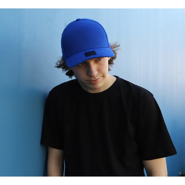 A blue cotton and spandex cap worn by a person in a black t-shirt, leaning against a blue wall.