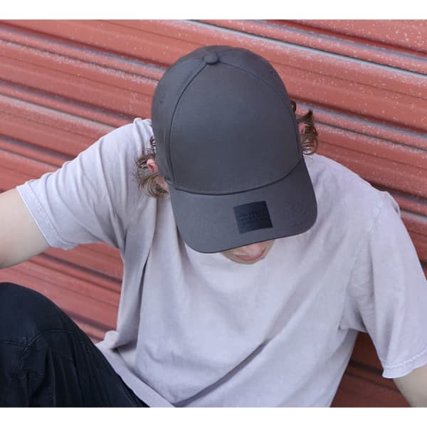 A grey cotton/spandex cap featuring a logo, worn by a person sitting against a red background.