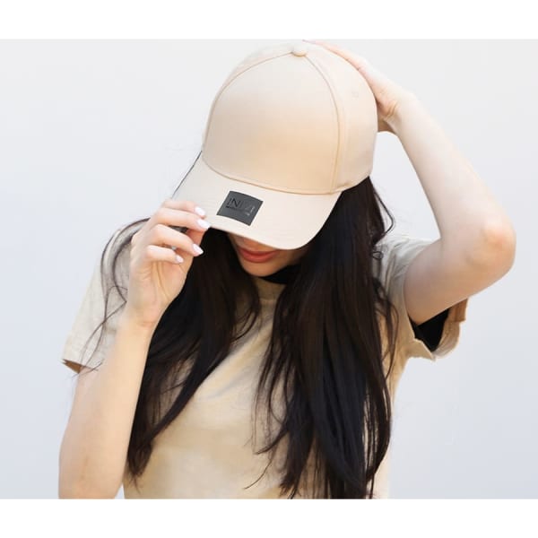 A beige cotton/spandex cap with a branded logo, worn by a person with long hair.