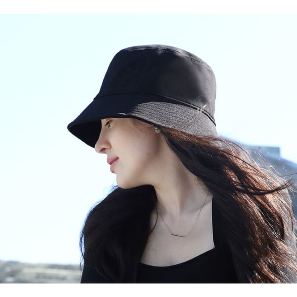 A woman wearing a black bucket hat with a wide brim, set against a bright outdoor background.