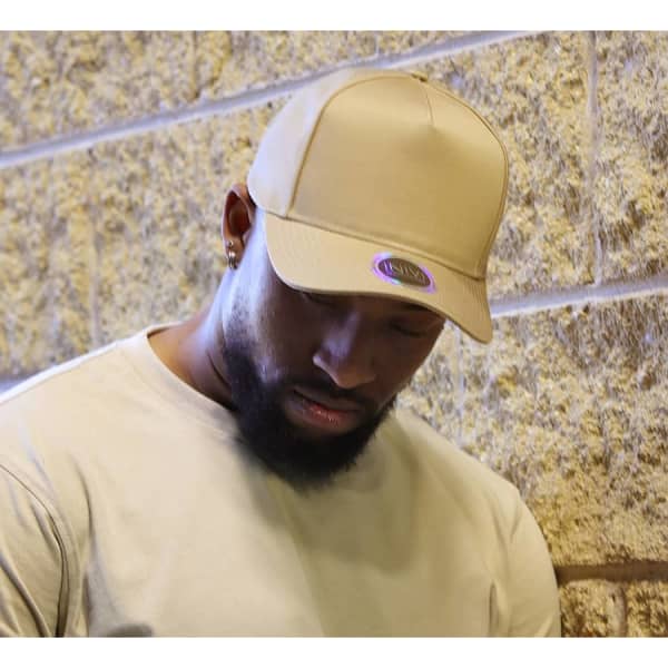 A beige cap is displayed on a model with a neutral background, featuring a branding logo.