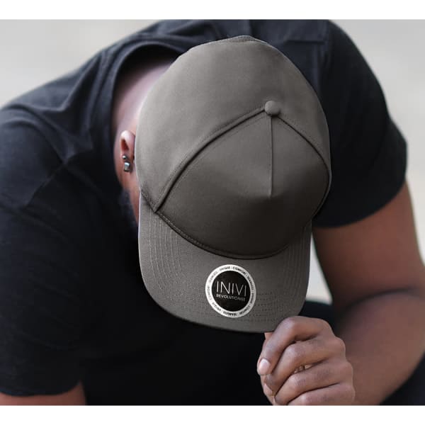 A grey cap with a round logo, resting on the head of a person wearing a black shirt.