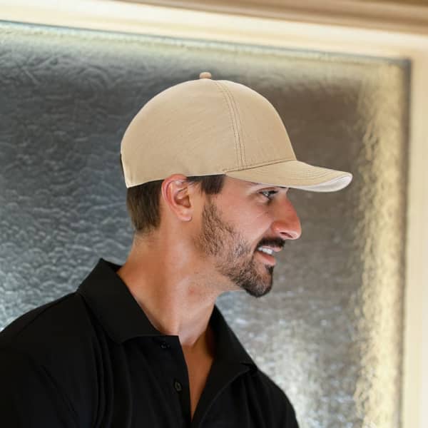A beige cap features a curved brim and a structured crown, positioned on a man’s head against a textured background.