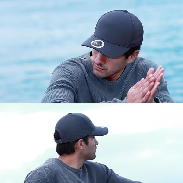 A grey bamboo cap with a logo, worn by a man looking away, set against a soft blue background.