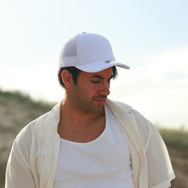 A man wearing a white mesh-backed cap and a light-coloured shirt, gazing downward in a natural setting.