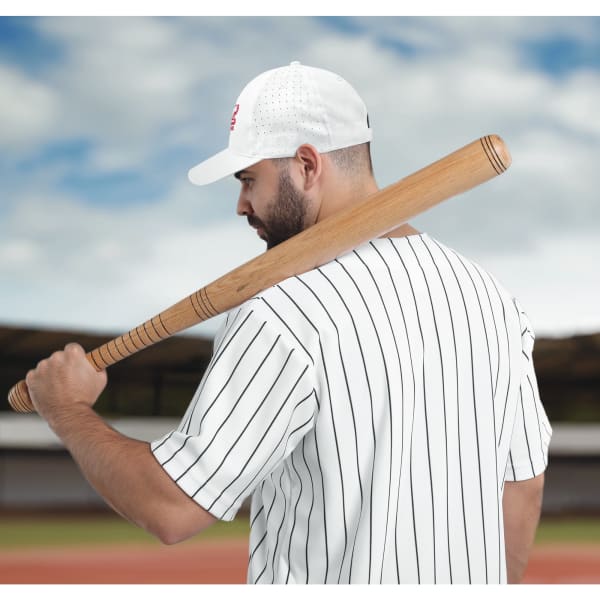 A man in a striped baseball jersey holds a wooden bat while wearing a white breathable cap with perforations.