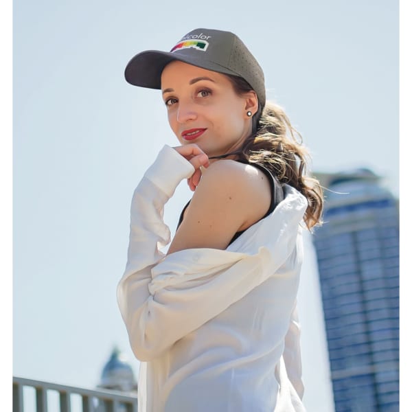 A woman poses outdoors wearing a grey breathable poly twill cap with circle perforations.