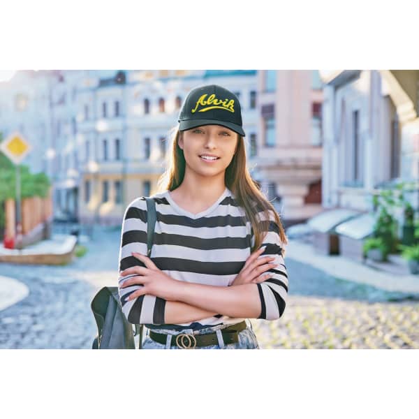 A cap in black with tear drop perforations, worn by a smiling young woman with long hair, standing in a street setting.