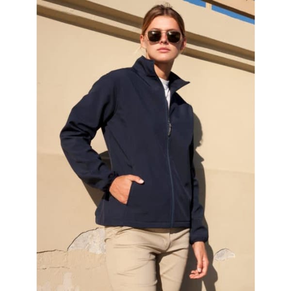 A navy soft shell jacket with a front zipper and side pockets, worn by a model in sunglasses.