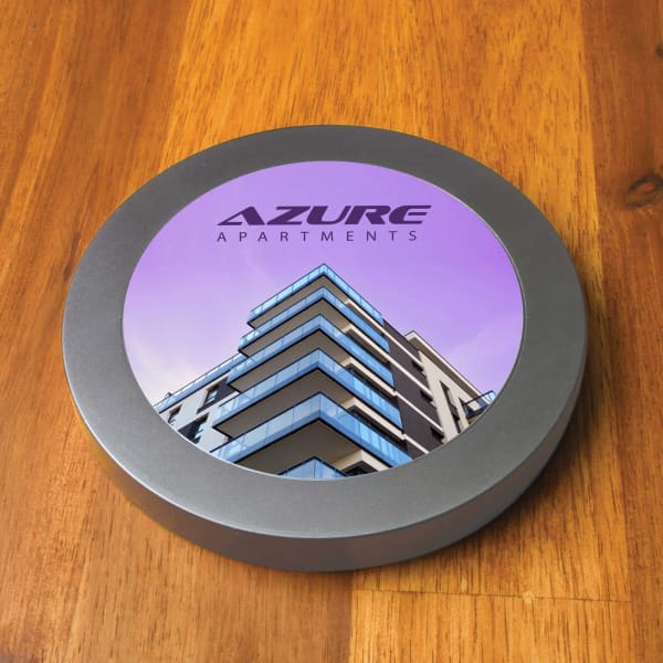 A round grey wireless charger featuring a graphic of a modern apartment building with blue accents.
