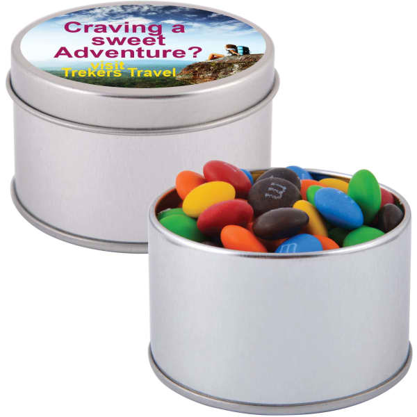 A silver round tin filled with colourful M&M's, including red, yellow, blue, green, and brown candies.