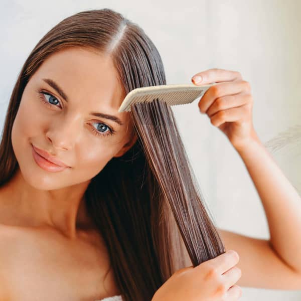 A woman with long, straight hair uses a light beige wheat fibre comb to style her hair.