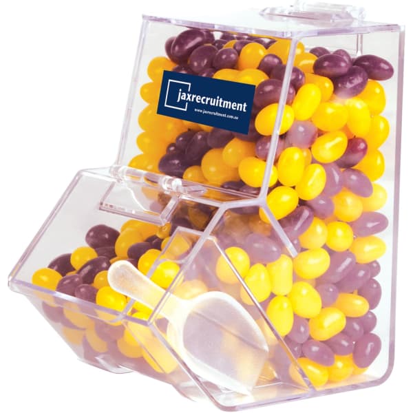 A clear dispenser filled with purple and yellow jelly beans, featuring a scoop and a branding logo.