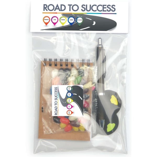 A gift pack containing a notebook, pen, colourful candies, and a key shape figure, all presented in a transparent bag.