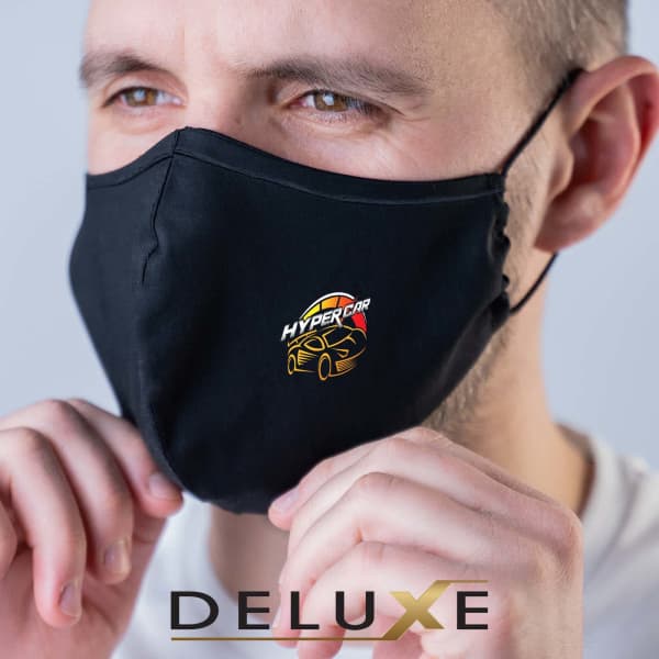 A black deluxe face mask with a logo, worn by a person holding the edges.