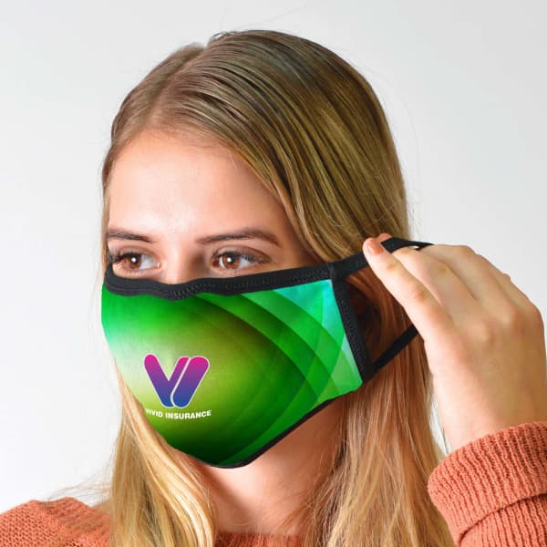 A green cotton face mask with a logo, being held by a person with long, blonde hair.