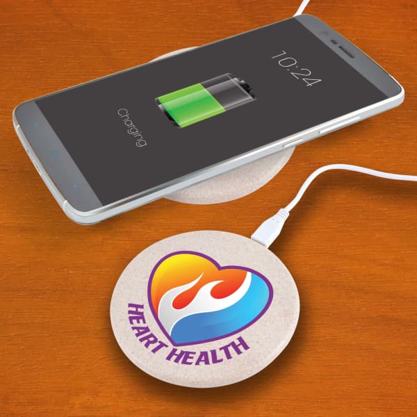 A round, natural-coloured wireless charger sits on a wooden surface next to a smartphone displaying a charging battery icon.
