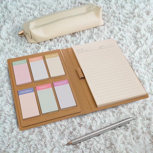 A Daily Note Planner with pastel sticky notes and a notepad in a tan cover, alongside a silver pen and a beige pencil case.