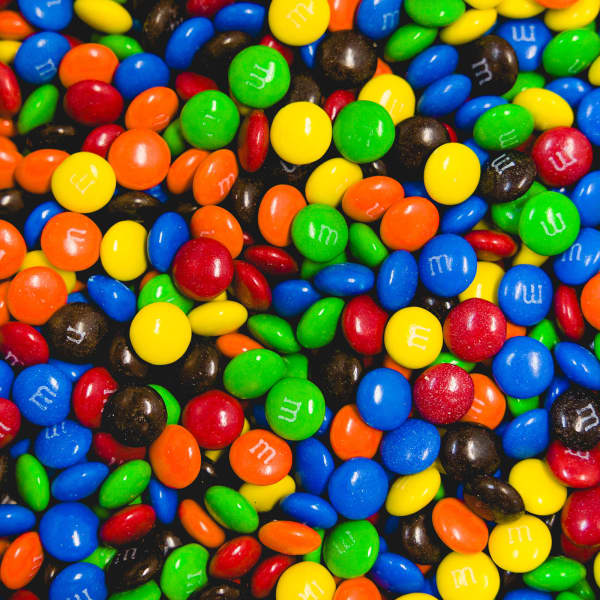 A colourful assortment of M&M's in red, yellow, blue, green, orange, and brown hues, featuring a logo.