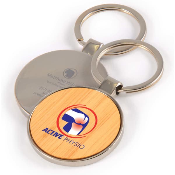 A circular bamboo keytag with a silver metal ring, featuring a logo on a wooden surface.