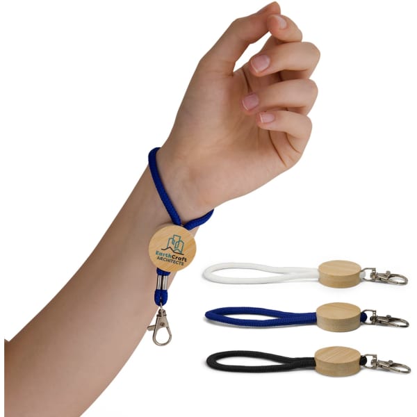 A hand is holding a blue Luxeloop Keytag, alongside white and black versions on a table. Each has a wooden circular attachment.