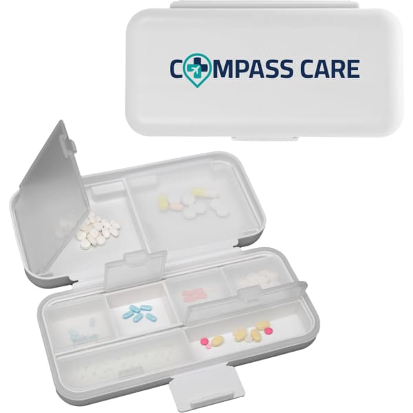 A compact white pill organiser with multiple compartments and a logo on the lid.
