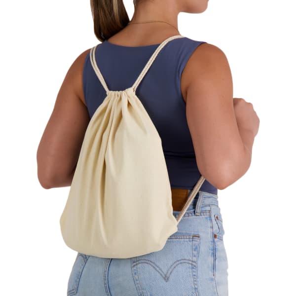 A cream drawstring backpack worn on the back, featuring soft fabric and rope straps.