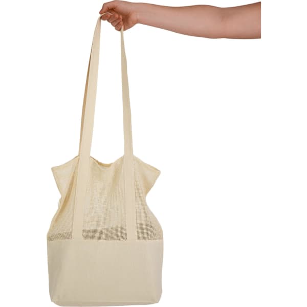 A cream-coloured tote bag with mesh detailing held by a hand, featuring long straps and a simple design.