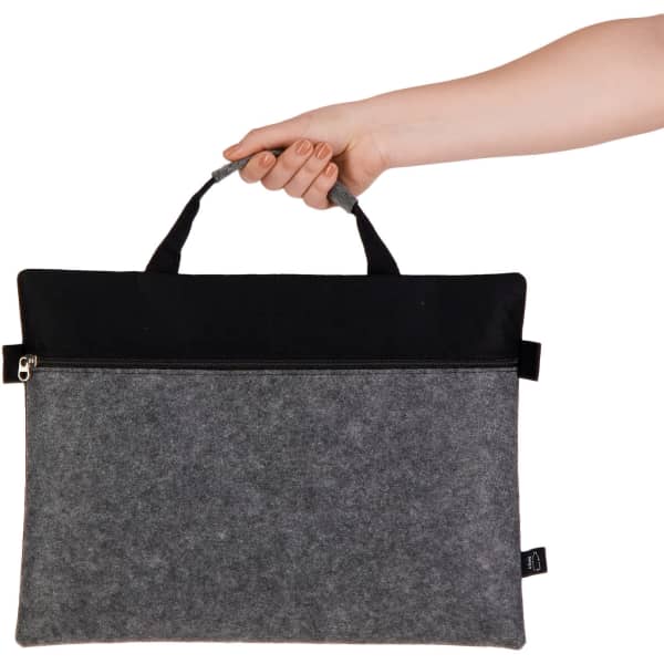 A hand holds a grey and black felt satchel with a zipper on top and two sturdy handles.