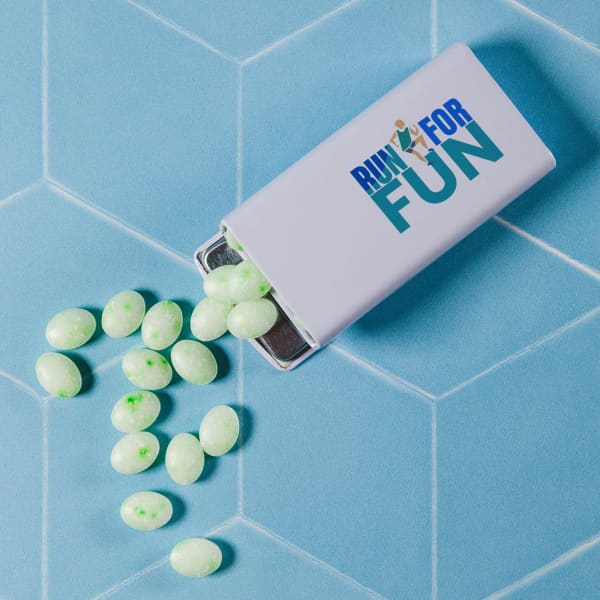 A flip-top tin containing spearmint mints, displaying green and white pills, on a geometric blue background.