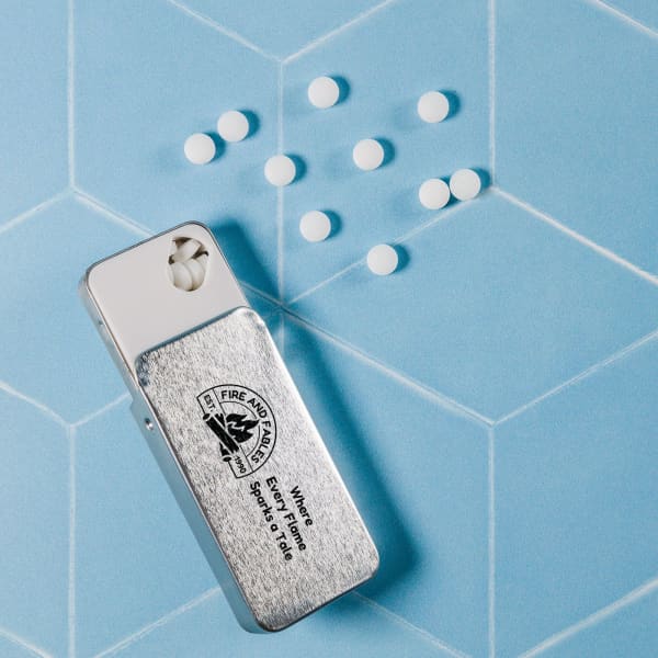 A silver slider tin containing small white sugar-free breath mints on a blue patterned background.