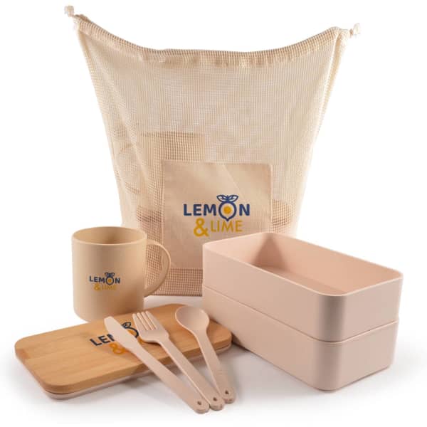 A beige mesh bag contains two pink food containers, a wooden tray, cutlery, and a beige mug, featuring a logo.