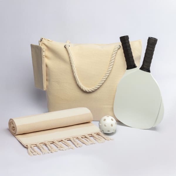 A cream carry bag, two paddle bats, a ball, and a cream towel with fringes. The bag features a rope handle.