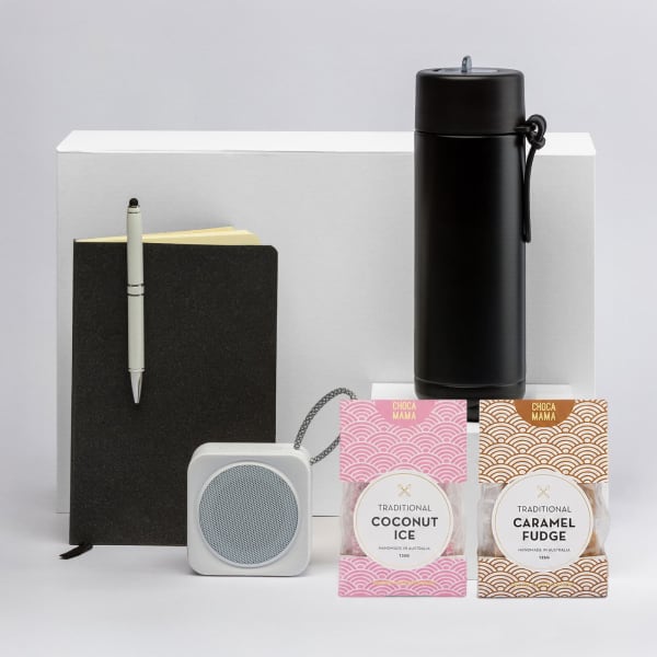 A black drink bottle, a grey portable speaker, a black notebook, and two packs of sweets: coconut ice and caramel fudge.