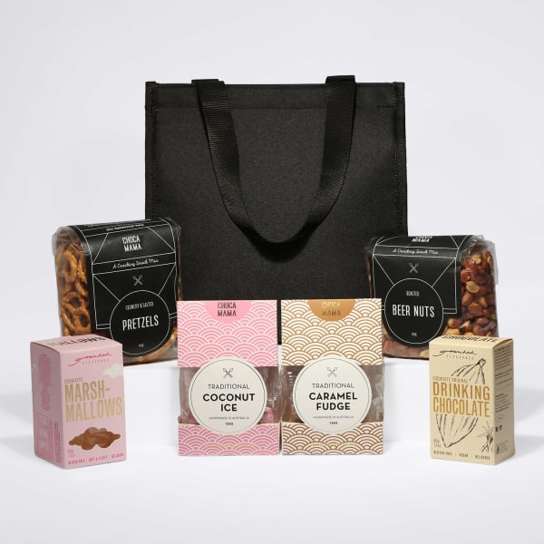 A black tote bag containing pretzels, beer nuts, marshmallows, coconut ice, caramel fudge, and drinking chocolate.