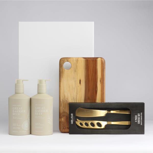 A wooden serving board, two cream bottles, and a boxed set of gold utensils on a grey background.