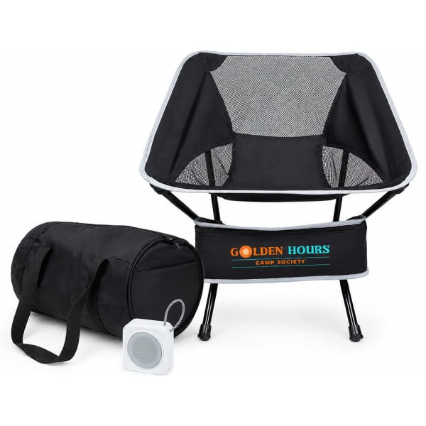 A portable camping chair in black fabric with a mesh backrest, accompanied by a carrying bag and a small speaker.