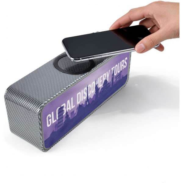 A grey speaker and inductive charger with a textured surface, featuring a hand placing a smartphone on top.