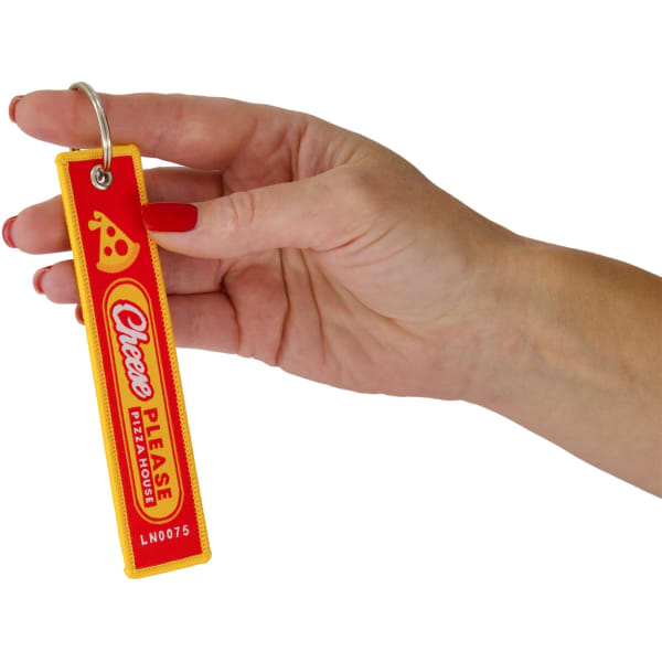 A hand holding a vibrant red and yellow woven keytag with a logo and text design.
