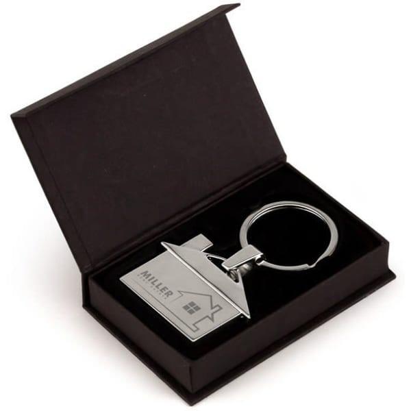 A silver keyring in the shape of a house, presented in a black gift box with a velvet interior.