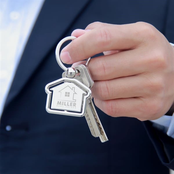 A silver keyring shaped like a house, held by a person in a suit, with keys attached.