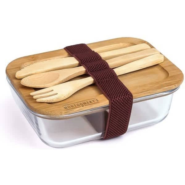 A glass lunch box with a bamboo lid, featuring wooden utensils and secured with a brown elastic strap.