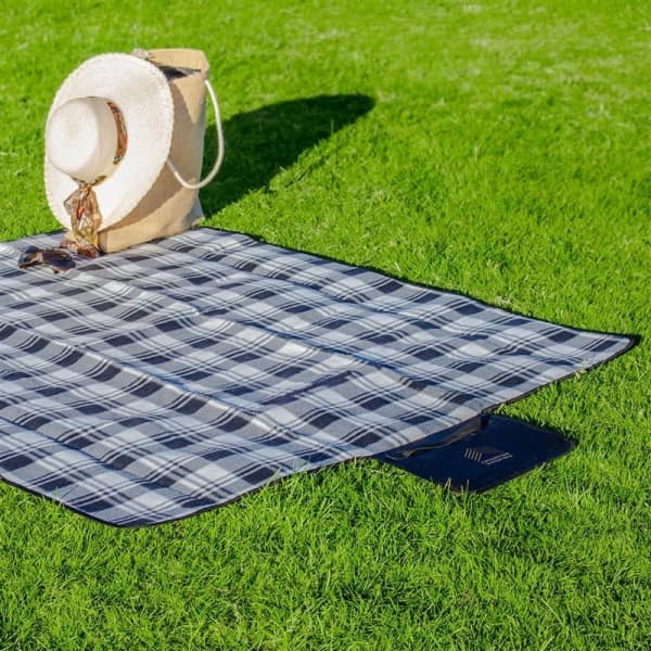 A plaid blanket in black and grey laid on green grass, with a straw hat and bag placed on top.