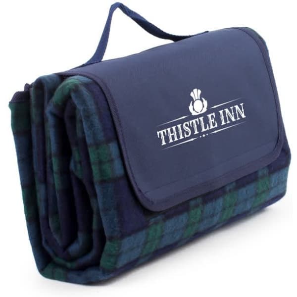 A folded navy and green tartan picnic blanket with a carry handle and a logo on the front.
