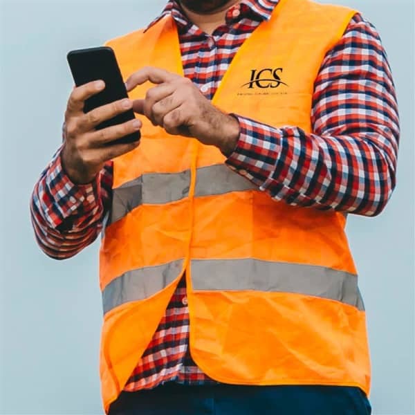 A man in a checked shirt is wearing a bright orange hi-viz vest with reflective stripes while using a smartphone.