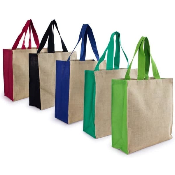 A range of Jute Carry All bags in red, black, blue, and green, featuring sturdy handles. Each bag has a beige body.