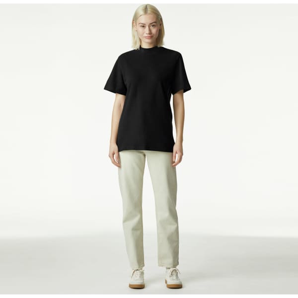 A black unisex pique mockneck sweater displayed on a model, paired with light-coloured trousers.