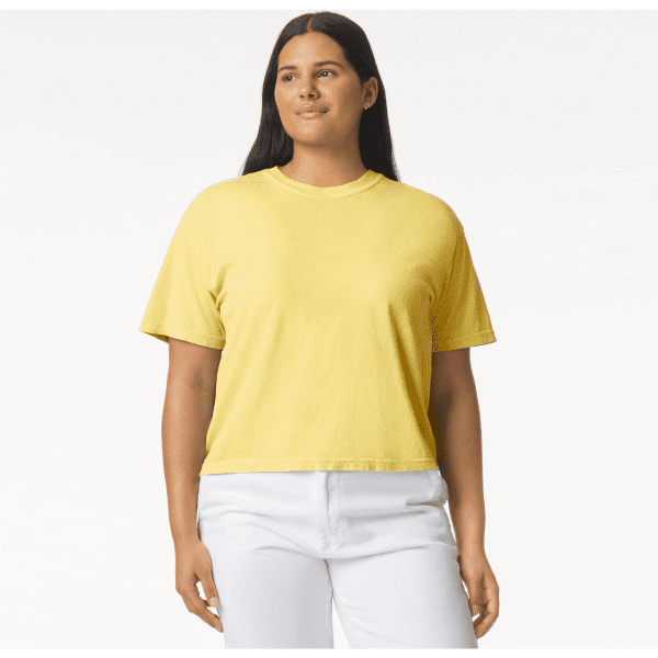 A woman wearing a yellow heavyweight boxy t-shirt, paired with white pants, standing against a simple background.