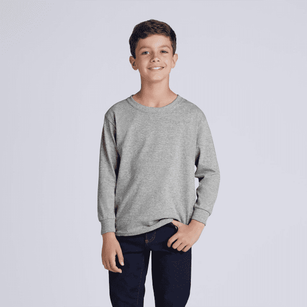 A grey heavy cotton youth long sleeve T-shirt displayed on a smiling child wearing dark jeans. The shirt features a logo.